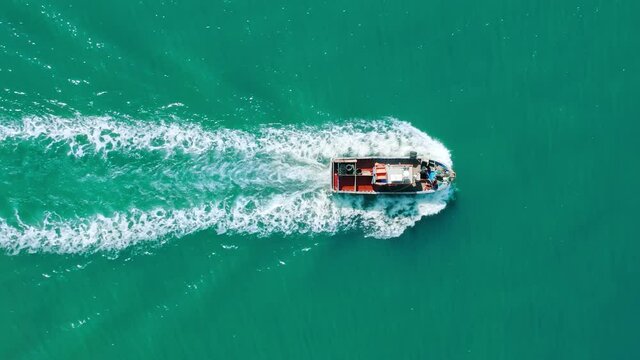 Aerial footage of a boat carrying cargo within turquoise ocean waters. A merchant ship sailing across the sea - view from above. High quality 4k footage