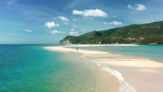Lingua areia, Portinho da Arrabida, Portugal. Aerial view of a man running across a narrow sandy path within the sea. Man runs along the coast with steep cliffs. High quality 4k footage