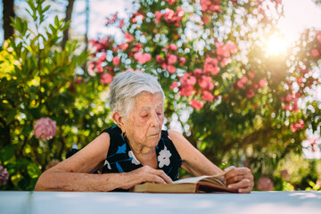 Elderly woman resting in the garden and reading a book
