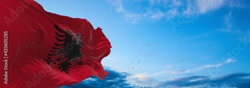 Large flag of Albania  waving in the wind on flagpole against the sky with clouds on sunny day. 3d illustration