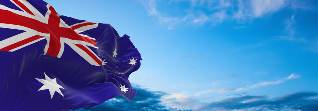 Large flag of Australia  waving in the wind on flagpole against the sky with clouds on sunny day. 3d illustration