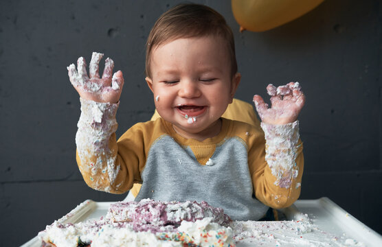 Baby boy laughing with smashed cake on his hands