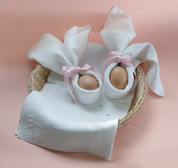 Minimalist Easter set with eggs in napkin bunny on a wicker basket on pink background.