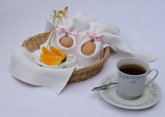 Beautiful festive Easter brunch with eggs in  napkin bunny, cup of tea, oranges and flowers on a basket.