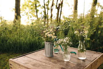 all sorts of wild cut flowers in vases on a wooden table in the garden