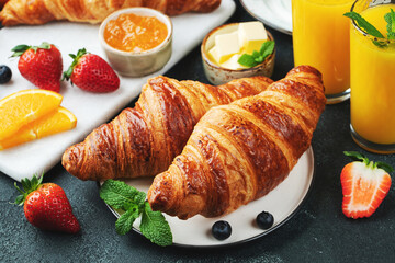 Fresh sweet croissants with butter and orange jam for breakfast. Continental breakfast on a black concrete table.