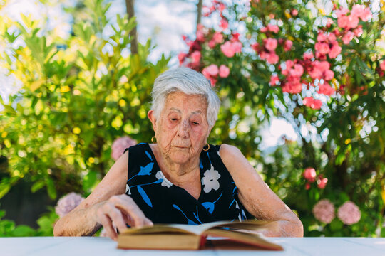 Elderly woman resting in the garden and reading a book