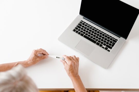 Unrecognizable senior woman with thermometer near laptop