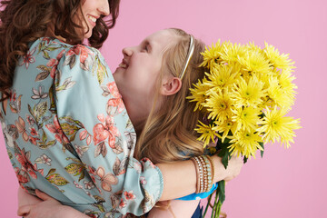 happy elegant mother and daughter embracing on pink