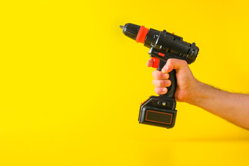 Cordless battery powered screwdriver on yellow background with cropped male hand holding tool for...