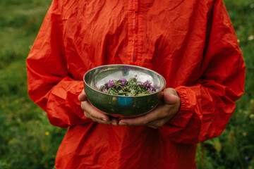 The girl in the bright raincoat holds a dish with flowers