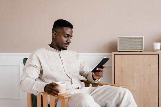 Positive young ethnic man with smartphone resting at home