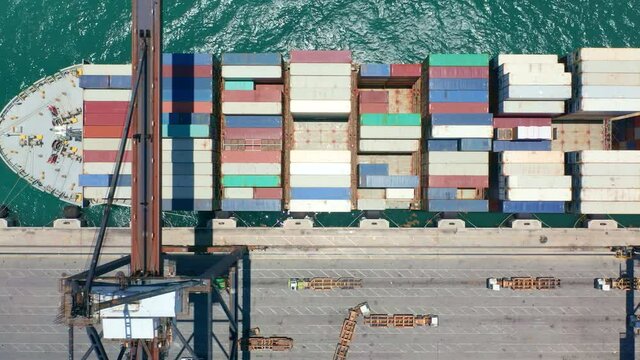 Vertical mobile video 9:16. Aerial top down view on unloading of cargo ship in port dock. Heavy shipping metal containers being loaded by industrial cranes. Water transportation, delivery business 4K