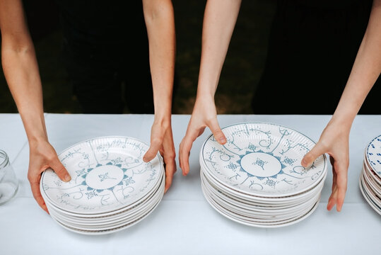 close up of two females placing a stack of porcelain plates on a table