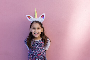 Adorable little girl wearing a unicorn headband with pink background