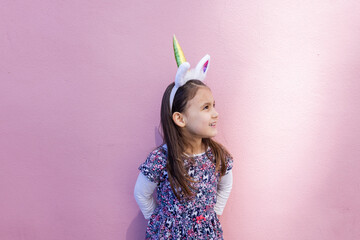 Adorable little girl wearing a unicorn headband with pink background