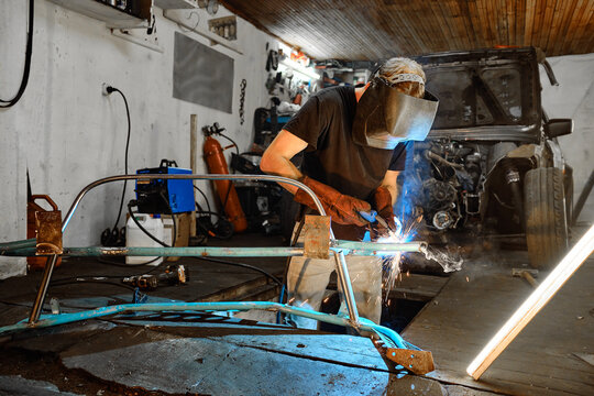 A man is engaged in welding work in a garage with a disassembled car