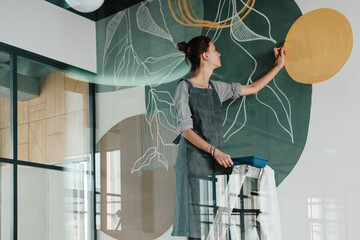 Young woman painting on wall behind glass