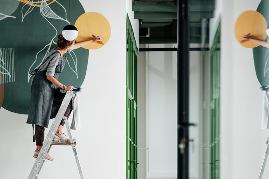 Young female painting on wall in new apartment