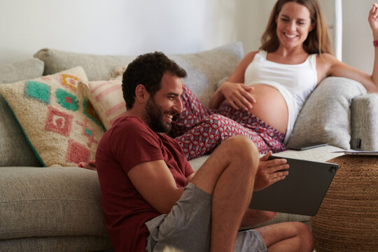 Delighted man showing tablet to pregnant woman