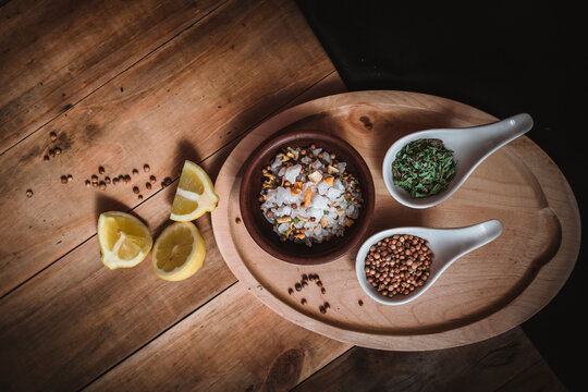 Ceramic posillo with salt and spices, lemon and coriander seeds, accompanied by spices, oregano and cut lemon, on wooden board and dark rustic background