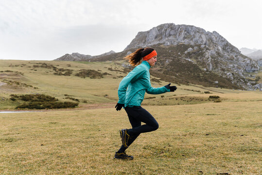 Sporty young woman running on green mountain hill in winter