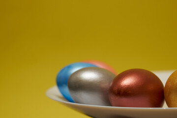 Painted eggs on a white plate with a yellow background.