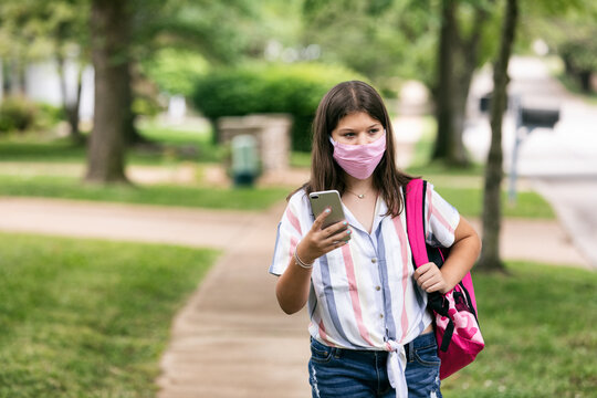 Student: Teen Girl With Face Mask Looks At Phone On Way To Schoo