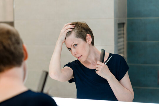 A woman gives herself a haircut at home.