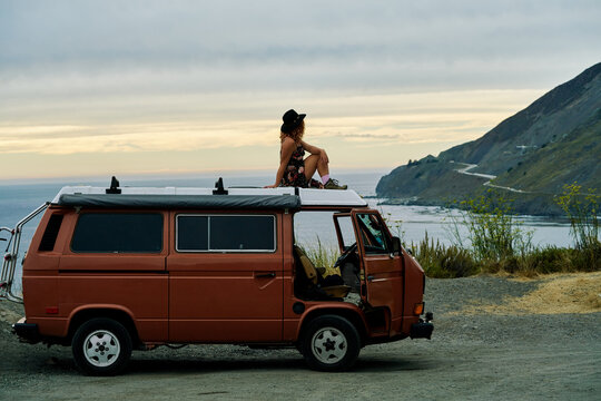 Young traveller enjoying the beautiful views of the Californian coast from the top of a vintage campervan.
