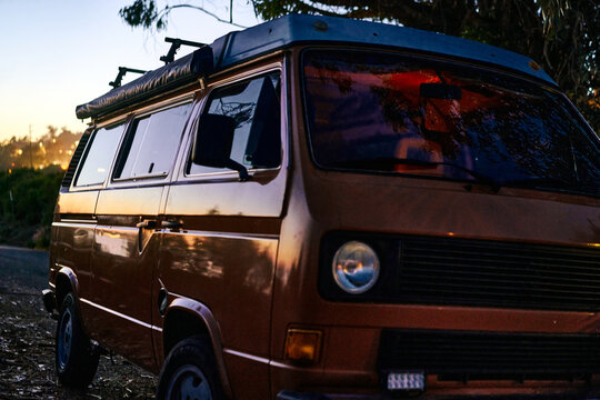 Vintage orange campervan parked during the night with a sunset reflection