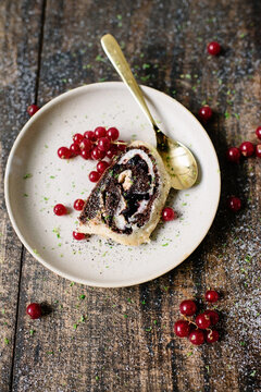 Piece of chocolate roll cake with red berries on a plate with golden spoon
