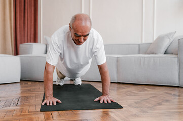 Positive aged man doing plank exercise at home