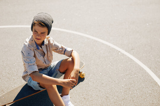 Kid Sitting On His Skateboard Outside