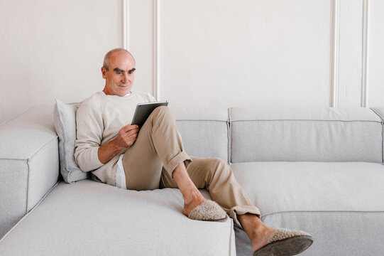 Senior man browsing tablet while resting on sofa