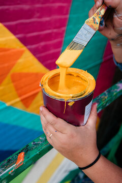 Artist Holding Paintbrush And Paint Can With Dripping Yellow Paint Next To A Geometric Colorful Wall Mural