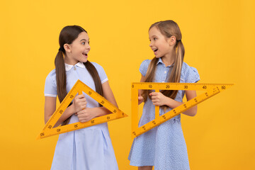 Happy school age children hold triangular rulers for geometry lesson, back to school
