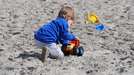 Red headed boy playing with Bucket spade and Digger on a sandy beach 