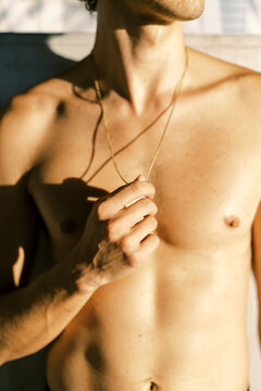Crop shirtless man touching pendant