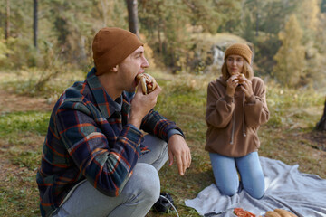 a man on a camping trip eats a hot dog for lunch and drinks coffee