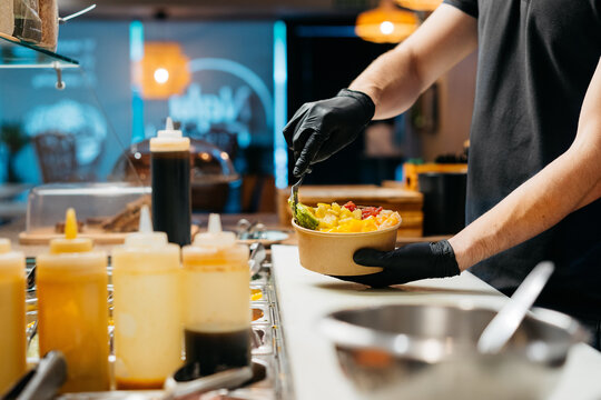 Anonymous waiter filling a poke bowl with food