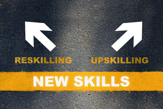 New skills development concept and changing skill demand idea. New skills written on yellow line with reskilling and upskilling with white arrow on asphalt road