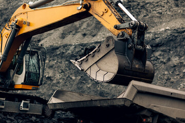 Excavator loads coal into the back of a heavy mining dump truck. Open pit coal mining.