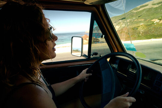 Young woman driving a vintage camper van though the Californian coast.
