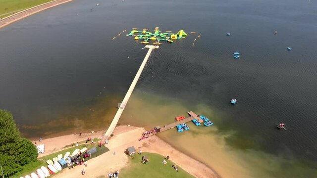 People having fun in Inflatable Water Park On Bewl Water Reservoir Lake during Sunny Day in Kent,Uk. Aerial flyover.