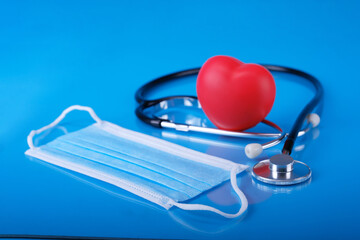 view of Stethoscope, red heart and two face mask on blue wood table. 