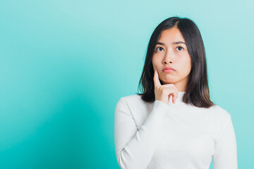 Fototapeta premium Young beautiful Asian woman hand near the face and thinking, Portrait female touch chin dream dreamy having doubts, studio shot isolated on a blue background
