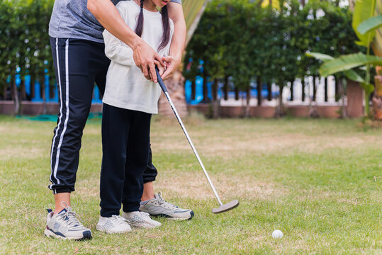 Asian young father support teaching training daughter to play perfect golf while standing in the game of golf together in nature a field garden park, family outdoors sport concept