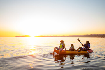 Father rows daughter and son in orange tandem kayak at sunset
