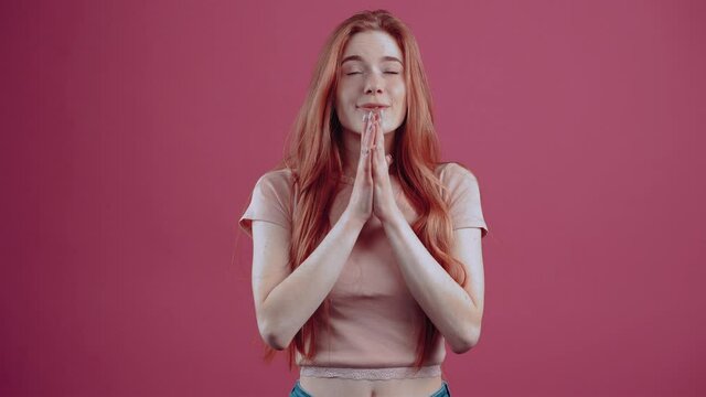 Suspended redhead young woman, in profile, 20 years old, in a pink casual T-shirt, isolated on a pink background. The concept of people's lifestyle. The freckled teenager with her fingers crossed